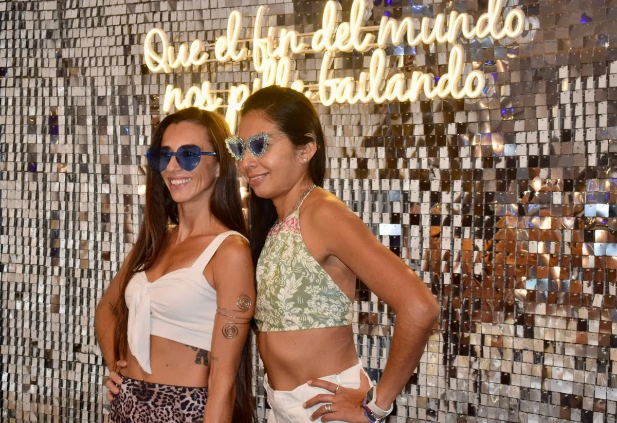 Dos amigas con gafas de corazón en la pared de lentejuelas