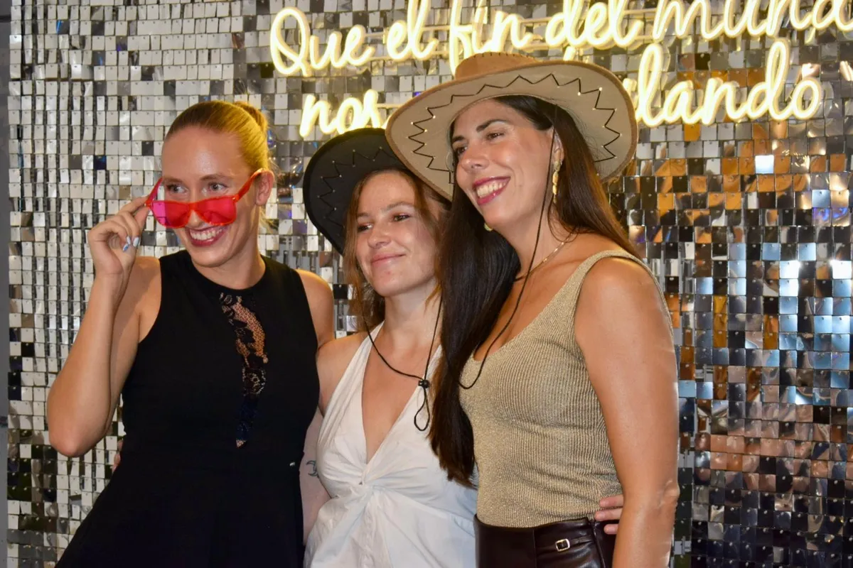 Invitadas con gafas y sombrero posando bajo el neón en Son Fusteret